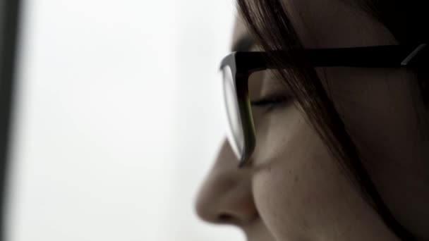 Extremo primer plano para el retrato de la cara femenina joven de perfil en gafas negras sobre fondo borroso y blanco. Hermosa mujer con su cara de perfil hablando y tocando su pelo corto y oscuro . — Vídeos de Stock