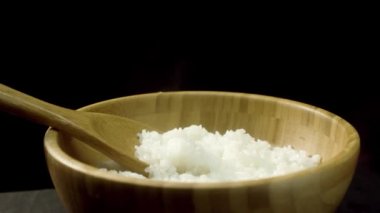 Bir ahşap kase haşlanmış pirinç için siyah arka plan üzerine izole ahşap karıştırma kaşıkla yakın çekim. Buhar büyük kaşıkla kavramı food yemek, derin, kahverengi plaka ile taze pişmiş pirinç.