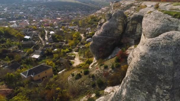 Blick von oben auf steinerne Klippen, die an der Stadt hängen. Schuss. Häuser im Tal, umgeben von Hügeln mit felsigen Klippen. Gefahr, in der Nähe von Felswänden zu leben — Stockvideo