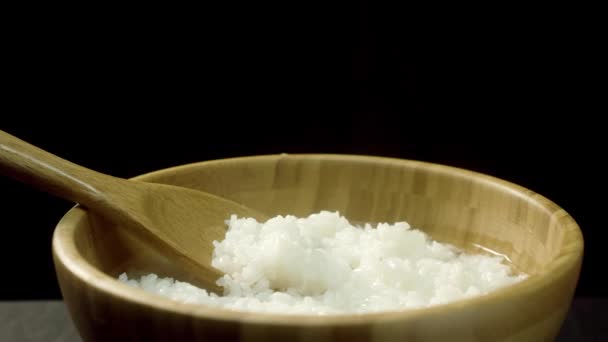 Kokta, yummy, heta ris med ånga i trä potten och stora sked, isolerad på svart bakgrund. Närbild för djup tallrik med kokt ris, hälsosam kost koncept. — Stockvideo