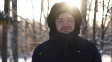 Bir siyah ceket kış ormanda kalmak ve kameraya bakarak kukuleta ile gülümseyen genç adam. Yakın çekim