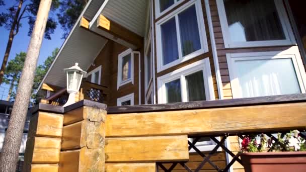 Close up for modern, two storey, wooden country house facade among green trees in a sunny day. Wooden summer cottage with many windows among green pines on blue sky background. — Stock Footage Close up for modern, two storey, wooden country house facade among green trees in a sunny day. Wooden summer cottage with many windows among green pines on blue sky background. Stock Video