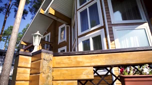 Close up for modern, two storey, wooden country house facade among green trees in a sunny day. Wooden summer cottage with many windows among green pines on blue sky background. — Stock Video