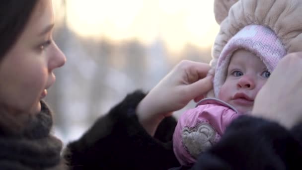 Close up for happy, beautiful mother touching the hat of lovely baby girl in winter park, family outdoors. Portrait of cheerful mommy with her cute child on a winter walk in the park. — Stock Video