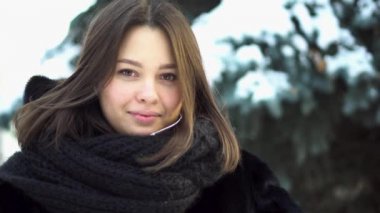 Genç, çekici kız bir kürk manto ve örme eşarp düz bir kış park, sokak moda arıyorsunuz için kapatın. Kış giysileri çam dalları arka plan üzerinde güzel kadın portresi.