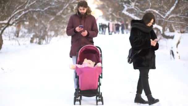 爸爸妈妈沉溺于手机, 忽视了婴儿车里的婴儿, 在冬季公园散步。家长们忙着智能手机忽视婴儿车里的小孩、毒瘾、价值观. — 图库视频影像