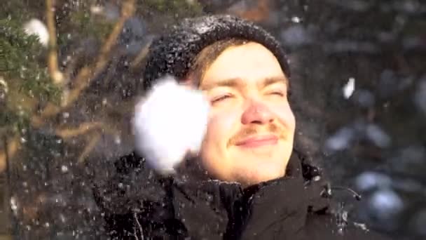 Portrait of young, smiling man with moustache enjoying snowfall in winter forest, squinting his eyes from the bright sun. Handsome, happy man likes falling snow over his head in winter sunny day. — Stock Video