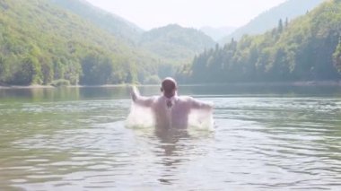 Tişörtlü adam dışarı su sıçramalarına ile atlar. Hisse senedi. Dağ gölde yüzmeye Beyaz tişörtlü adam. Gölün yanında dağlarda yaz tatili
