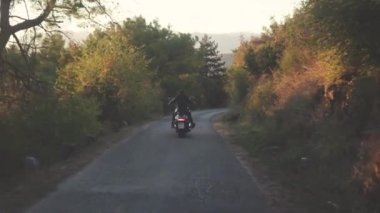 Gelen orman yolu üzerinde motosiklet kişini arkasında görüntüleyin. Hisse senedi. Motosikletçi yol virajlı asfalt üzerinde sürme siyah deri ceketli görünümünü arka. Güneşli günde yoğun yeşil orman üzerinden yolculuk motosiklet