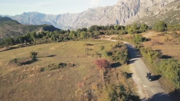 Motociclista montando en carretera rural en las montañas. Acciones. Vista superior de motociclista en chaqueta de cuero negro en motocicleta de alta velocidad. Viaje en moto entre montañas en verano — Vídeo de stock