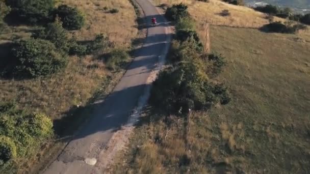 Par ridning motorcykel på lantlig väg. Lager. Ovanifrån av ridning motorcyklist och hans kvinna i röd klänning. Romantisk resa på motorcykel på sommaren — Stockvideo