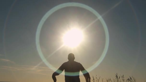 Achteraanzicht van de mens verhogen zijn handen aan zon. Voorraad. Mens in lang shirt bidt op gebied bij zonsopgang. Zon-aanbidding — Stockvideo