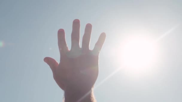 Close-up of hand reaching for sun. Stock. Bright sunlight breaks through fingers of outstretched hand to sky — Stock Video