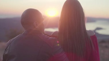 Çift birbirlerine batımını Close-up. Hisse senedi. Deri ceketli adamı kırmızı elbiseli çekici kadın sevgiyle bakar. Gün batımında dağ nehir manzaralı romantik tarih