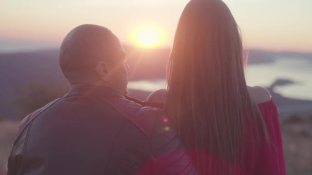 Primo piano di coppia che si guarda al tramonto. Azioni. Uomo in giacca di pelle guarda con amore la donna attraente in abito rosso. Appuntamento romantico con vista fiume montagna al tramonto — Video Stock