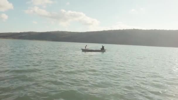 Ovanifrån av båt med två män i havet. Lager. Två män i träbåt drunkning på bakgrund av berg och blå himmel — Stockvideo