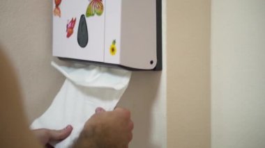 Banyoda çiçek ve kelebek çıkartma ile beyaz plastik kutusundan doku çekerek adam eller için kapatın. Beyaz kağıt havlu dispenseri su dolabı ve bu kağıt alarak adam ellerini duvara.