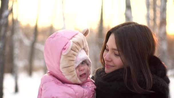 近距离描绘婴儿和她年轻, 美丽的母亲在雪树外的冬季公园背景。快乐的母亲微笑着, 享受寒冷的一天, 看着她可爱的宝宝. — 图库视频影像