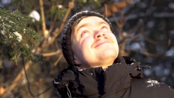 Ritratto di giovane, uomo sorridente con i baffi alza gli occhi, gode di nevicate nella foresta invernale, strizza gli occhi dal sole luminoso. Bello, uomo felice piace cadere neve sopra la testa in una giornata di sole . — Video Stock