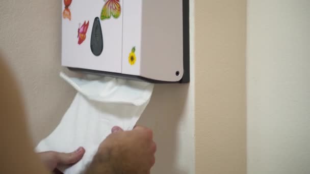 Close up for man hands pulling tissues from white plastic box with flower and butterfly stickers in bathroom. White paper towel dispenser on the wall in water closet and man hands taking this paper. — Stock Video