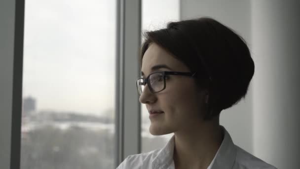 Mujer de negocios en camisa blanca de pie cerca de la ventana y relajarse en la oficina. Primer plano . — Vídeos de Stock