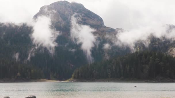 Paisaje de montañas y lagos con nubes. Acciones. Montaña con denso bosque verde cerca de lago azul con nubes bajas en clima nublado. Misterioso paisaje nublado de montaña — Vídeos de Stock