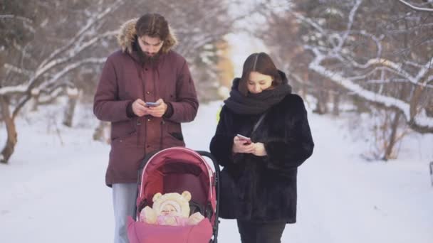 Couple dans les téléphones pour marcher. Couple moderne avec bébé avec téléphones ne remarquez pas l'autre sur la promenade dans le parc en hiver. Relations des personnes modernes s'éloignant dans les smartphones — Video