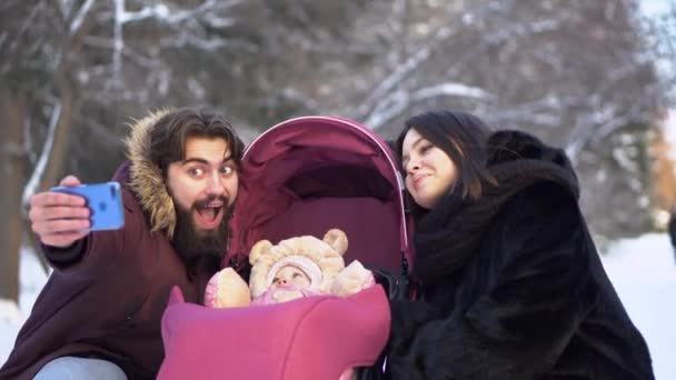 Casal com bebê tirar selfie na caminhada. O par casado jovem com o bebê no carrinho toma a selfie no passeio no inverno. Jovens modernos família feliz — Vídeo de Stock