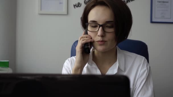 Närbild av sekreterare med leende prata telefon. Attraktiv ung kvinna prata telefon i office — Stockvideo