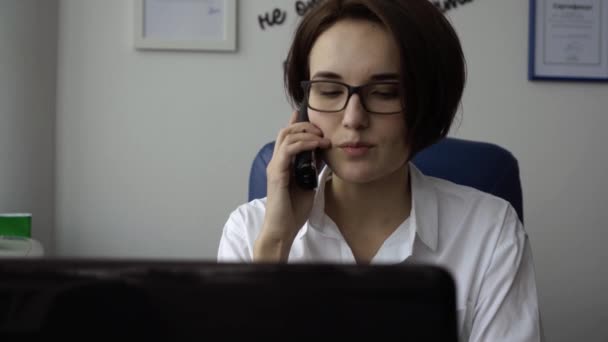 Primer plano de la secretaria con sonrisa hablando por teléfono. Atractiva joven mujer hablando por teléfono en la oficina — Vídeos de Stock