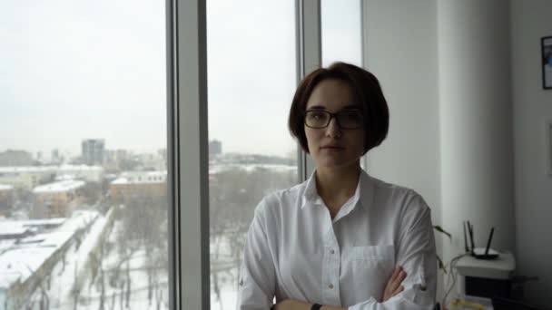 Joven mujer de negocios con los brazos cruzados en la ventana de fondo. Retrato de joven empresaria confiada en gafas con las manos cruzadas mirando al trabajador — Vídeo de stock