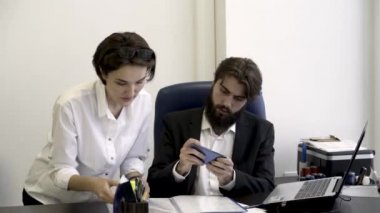 Kadın Sekreter ofiste, modern cihazlarla kavramı bağımlılığı akıllı telefon oyun ile meşgul sakallı patronu için önemli belgeleri gösterir. İşadamı öfkeyle kağıtları imzalar.