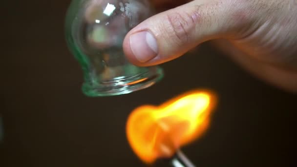 Close up for cupping therapist hand heating up a cupping glass with a flame, isolated on black background. Acupuncturist heating a cupping bulb with a flame, spa, relaxation concept. — Stock Video