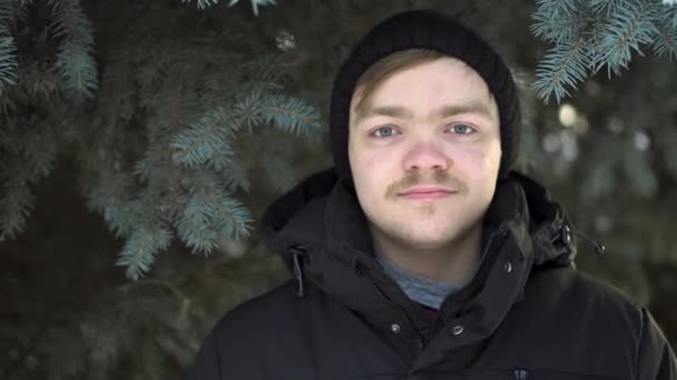 Portrait of a blond man with moustache in warm clothes over green spruce background. Close up for young man standing in winter forest against Christmass tree. — Stock Video