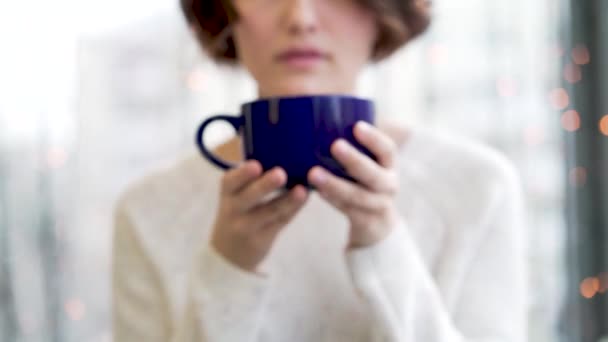 Chica ambiente acogedor con gran taza de café cacao chocolate Navidad invierno. Cerca de las manos de las mujeres jóvenes sosteniendo una gran taza de bebida caliente. Mujer usando suéter de punto blanco de gran tamaño de moda — Vídeo de stock