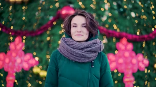 Hermosa mujer joven linda con una bufanda en la calle en el fondo del árbol de Navidad. Estilo urbano — Vídeo de stock