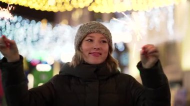 Bir kızla bir maytap onun elinde. Noel kartı. Parlak kış arka plan ile altın ışık. Maytap şehir çelenk arka plan üzerinde onun elinde olan güzel kadın