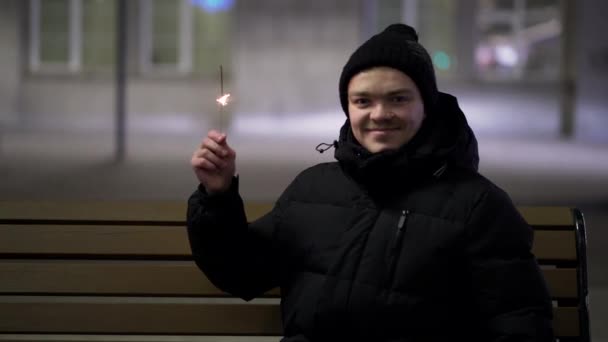 Jonge man zitten in de stad met wonderkaarsen. Kerstsfeer. Wonderkaarsen in de handen van een vent — Stockvideo