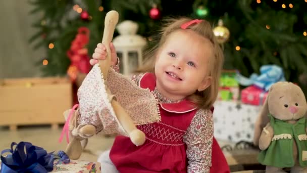 Muy agradable niña encantadora en jaket rojo. Niña jugando con juguetes en el fondo del árbol de Navidad — Vídeos de Stock