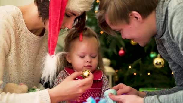 Una familia feliz con un niño pasa la Navidad juntos. Los padres y la hija juegan en casa cerca del árbol de Navidad — Vídeos de Stock