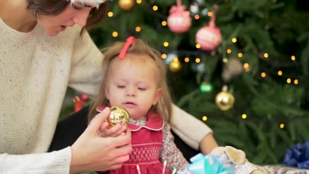 Mutlu anne Noel ağacının yanında oynayan küçük kızıyla birlikte. Güzel anne ile şenlikli Noel ağacı yakın bir sandalyede oturan küçük kızının oynarken — Stok video