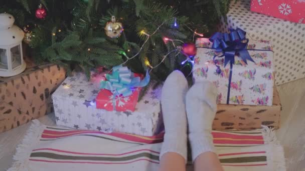 Close-up. Pés de mulher em meias de Natal perto da árvore de Natal. Férias. Pés das mulheres na árvore de Natal e presentes fundo — Vídeo de Stock