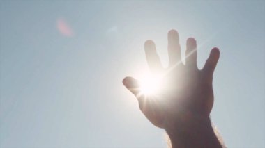 Güneş için ulaşan el Close-up. Hisse senedi. Parlak güneş ışığı uzanmış el parmaklarının arasından göğe tatili.