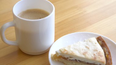 Beyaz kupa ve peynirli kek ile plaka Close-up. Sabah kahvaltı kahve ve ahşap masa üzerinde klasik cheesecake