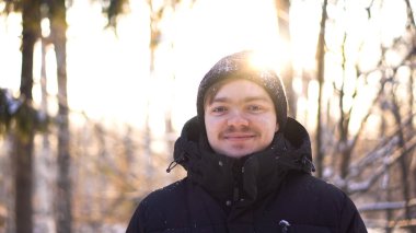 Güneş ışığı arka plan üzerinde genç adam Close-up. Güneş ışığı grove kışın yapmak arka planda gülümseyen genç çekici adam