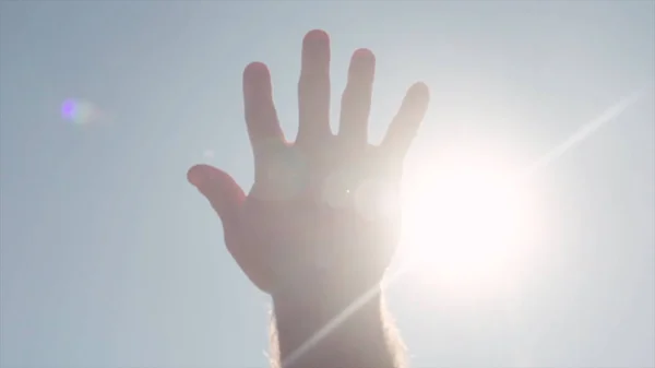 Close-up of hand reaching for sun. Stock. Bright sunlight breaks through fingers of outstretched hand to sky