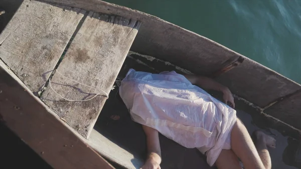 Man lying in boat. Stock. Naked man lying covered with white blanket in wooden boat with water on bottom. Corpse in wooden boat