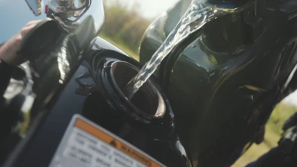 Fechar de encher motocicleta gasolina. Estoque. Close-up de reflexão do homem no detalhe cromado da motocicleta. Motociclista derrama gasolina da lata em tanque. Abastecimento antes de continuar a viagem — Fotografia de Stock