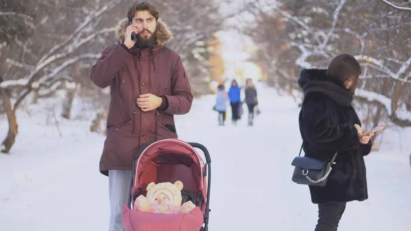 Couple in phones for walk. Modern couple with baby with phones dont notice each other on walk in park in winter. Relations of modern people moving away in smartphones