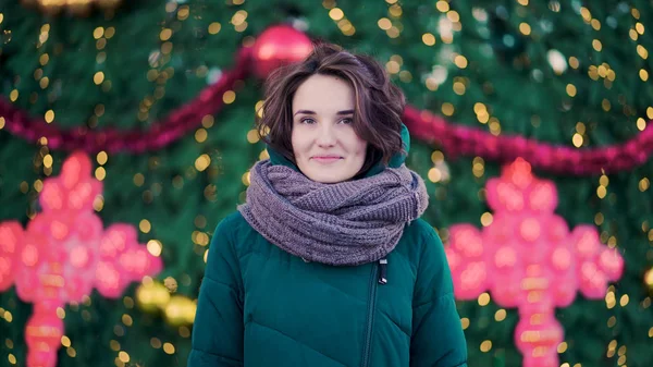 Bella giovane donna carina con una sciarpa sulla strada sullo sfondo dell'albero di Natale. Stile urbano — Foto Stock